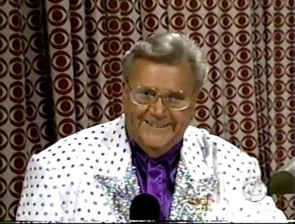 Rod is wearing a white jacket with silver dots and silver lapels & a purple collarless silk shirt