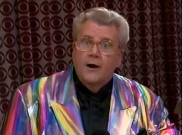 Rod is wearing a shiny purple-red-pink-yellow-blue-green jacket & black collarless silk shirt