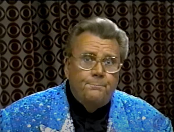 Rod is wearing a blue jacket with large sequins & silver lapels & a black silk collarless shirt
