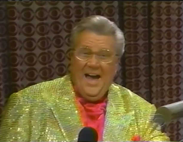 Rod is wearing a gold sequined jacket, salmon pocket square & salmon silk collarless shirt