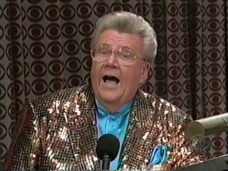 Rod is wearing a shiny brown jacket with black sequins & a teal collarless silk shirt with matching pocket square