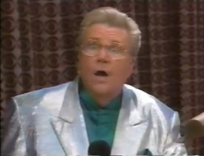 Rod is wearing a silver jacket & a dark-green collarless silk shirt with matching pocket square