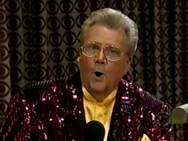 Rod is wearing a dark-red sequined jacket & yellow collarless silk shirt with matching pocket square