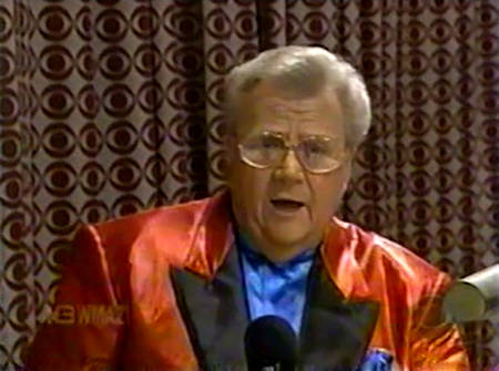 Rod is wearing a shiny red jacket with black lapels jacket & blue collarless silk shirt with matching pocket square