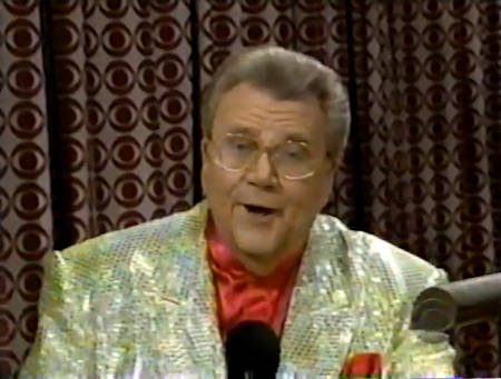 Rod is wearing a gold sequined jacket & red collarless silk shirt with matching pocket square