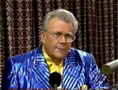 Rod is wearing a shiny blue/blue-striped jacket, yellow collarless silk shirt w/ matching pocket square