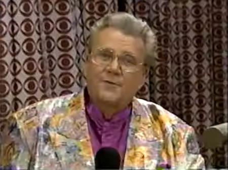 Rod is wearing a shiny pastel-colored/patterned jacket & purple collarless silk shirt with matching pocket square