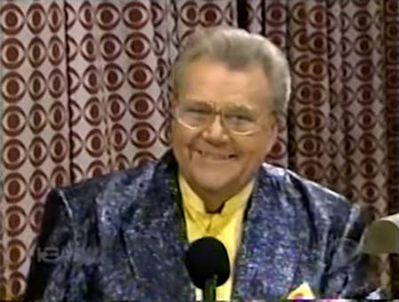 Rod is wearing a purpleish-blue sequined jacket & yellow collarless silk shirt with matching pocket square
