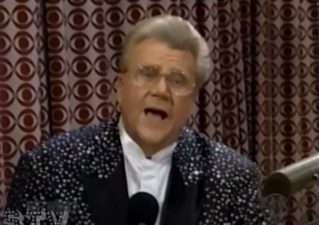 Rod is wearing a black jacket with white speckles, black lapels & white collarless silk shirt