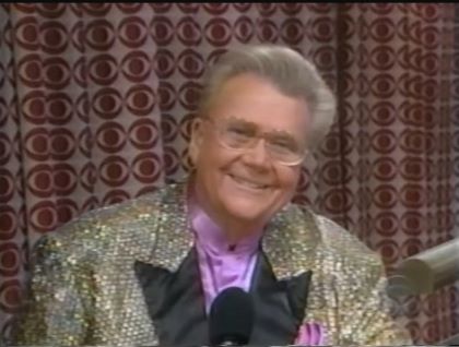 Rod is wearing a gold sequined jacket with black lapels & a violet collarless silk shirt with matching pocket square