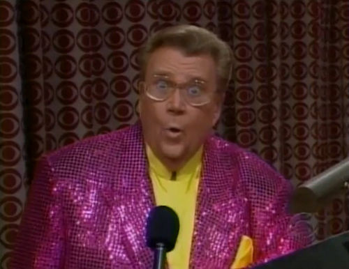 Rod is wearing a purple-pink sequined jacket & yellow collarless silk shirt with matching pocket square