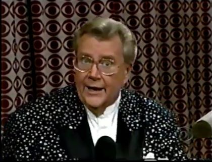 Rod is wearing a black jacket with white specks and black lapels & a white collarless silk shirt with matching pocket square