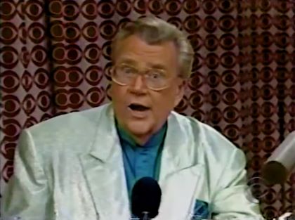 Rod is wearing a shiny gray/green jacket & seafoam green collarless silk shirt with matching pocket square