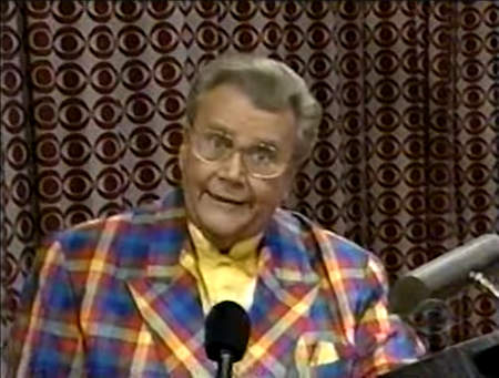 Rod is wearing a red-blue-yellow gingham jacket & yellow collarless silk shirt with matching pocket square