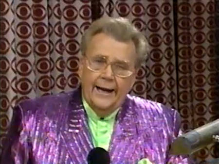 Rod is wearing a shiny purple/purple-striped jacket & lime-green collarless silk shirt with matching pocket square
