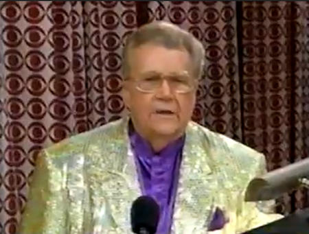 Rod is wearing a gold sequined jacket & purple collarless silk shirt with matching pocket square