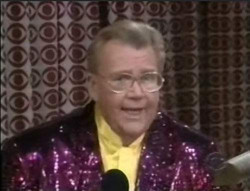 Rod is wearing a purple sequined jacket & yellow collarless silk shirt