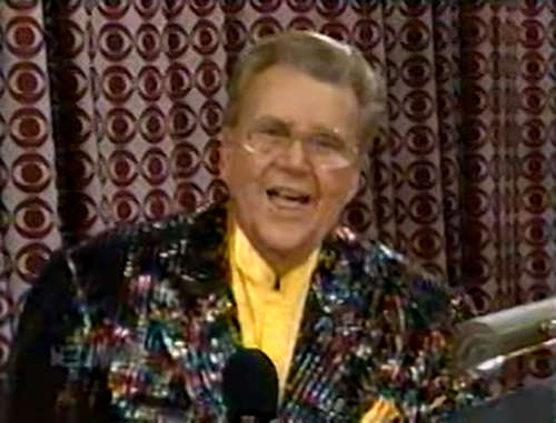 Rod is wearing a multi-colored sequined jacket & yellow collarless silk shirt with matching pocket square