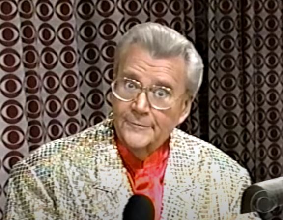 Rod is wearing a gold shimmery jacket & red silk collarless shirt