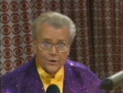 Rod is wearing a purple sequined jacket & yellow collarless silk shirt with matching pocket square