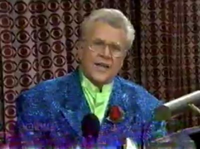 Rod is wearing a blue sequined jacket with a red rose & lime green collarless shirt 