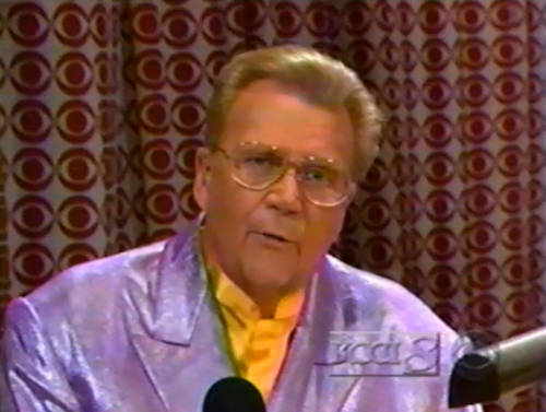 Rod is wearing a shiny purple jacket & yellow collarless silk shirt