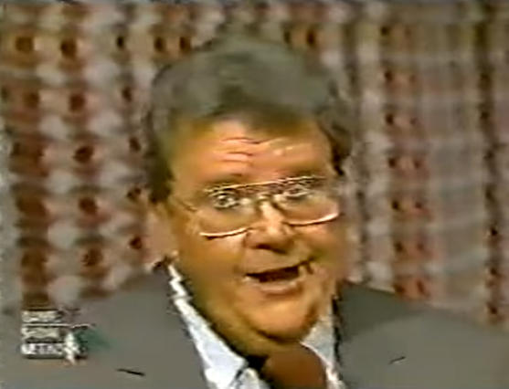 Rod is wearing a taupe jacket, a white shirt & a necktie