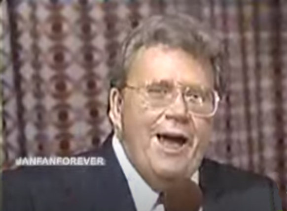 Rod is wearing a black suit jacket & red tie with a white shirt