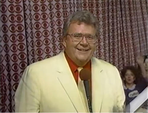 Rod is wearing a cream-colored jacket, matching neck tie & a red shirt