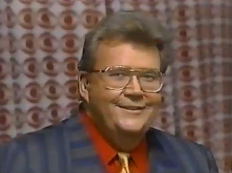 Rod is wearing a grey & blue striped jacket, gold tie & red shirt