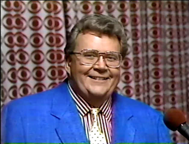 Rod is wearing a blue jacket, yellow neck-tie with red polka dots & a red and white-striped shirt