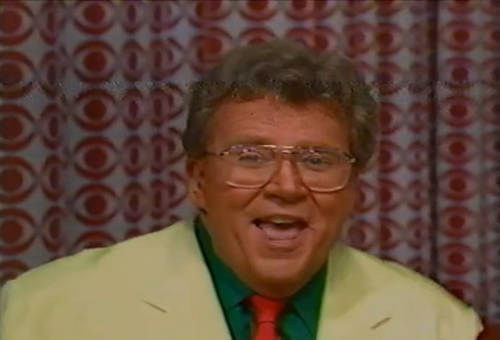 Rod is wearing a cream jacket, green shirt and a red silk necktie