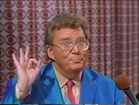 Rod is wearing a blue jacket, blue & red necktie & tan shirt