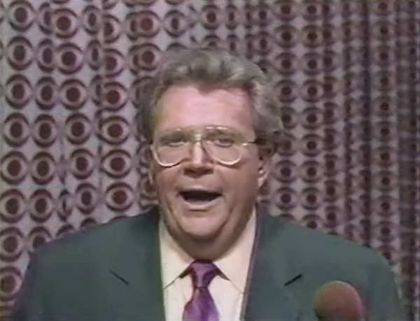 Rod is wearing a dark-green jacket, purple neck tie & cream shirt