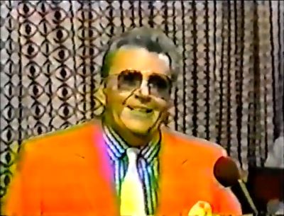 Rod is wearing an orange jacket, yellow necktie with matching pocket square & a blue & white-striped shirt