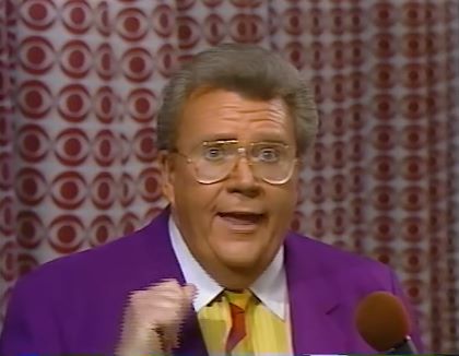 Rod is wearing a purple jacket, multi-colored-striped neck tie & a yellow shirt a white collar