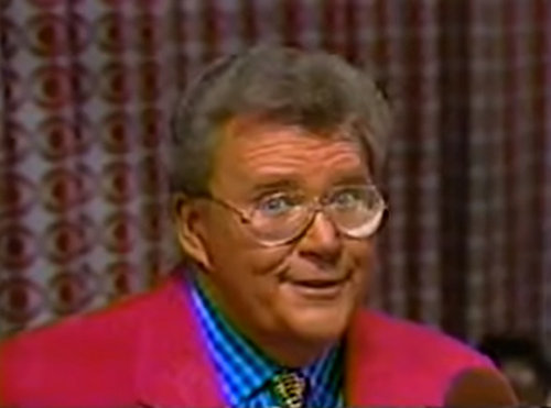 Rod is wearing a fuchsia jacket, yellow patterned tie & blue gingham shirt