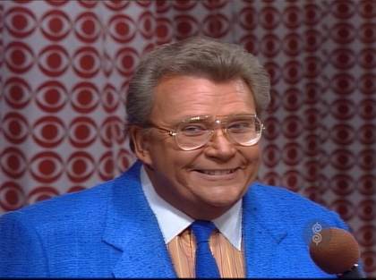 Rod is wearing a blue jacket with matching necktie and a tan shirt with stripes & a white collar