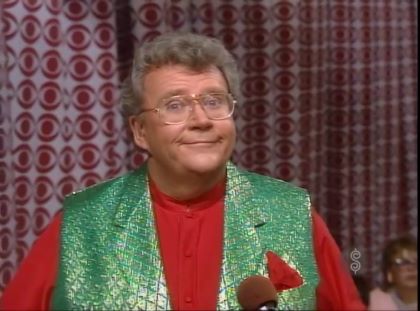 Rod is wearing a shiny green-quilted vest, red collarless silk shirt & matching pocket square