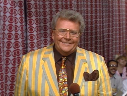 Rod is wearing a gold & gray striped jacket, brown shirt with matching pocket square & patterned necktie