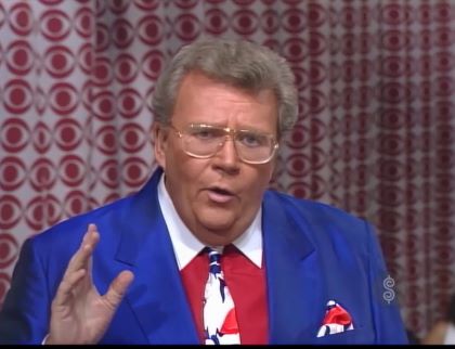 Rod is wearing a blue jacket, red shirt with a white collar, mottled neck-tie & matching pocketsquare