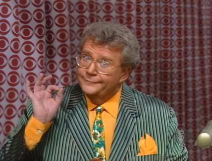 Rod is wearing a green/black/grey pin-striped jacket, patterned neck tie & mustard-yellow shirt with matching pocket square