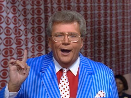 Rod is wearing a blue/blue striped jacket, a red shirt with white collar and a white necktie with red polka dots with matching pocket square