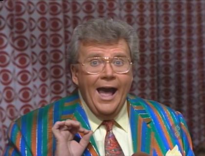 Rod is wearing a blue/green/orange striped jacket, cream shirt with matching pocket square and a mottled necktie