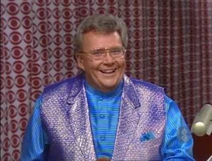 Rod is wearing a shiny purple vest and a blue-blue horizontally striped silk shirt with matching pocket square