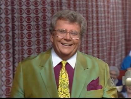 Rod is wearing a silk golden-green jacket, maroon shirt with white collar, yellow/maroon necktie & a maroon pocket square