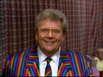Rod is wearing a rainbow-striped jacket, matching necktie & white shirt