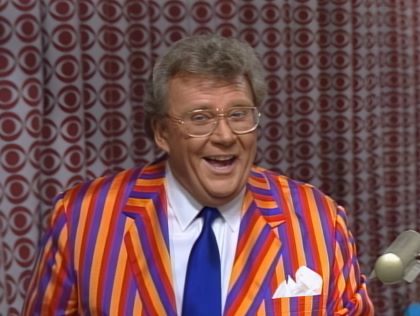 Rod is wearing a purple/red/orange striped jacket, blue necktie & white shirt with matching pocket square