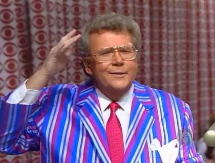 Rod is wearing a blue/silver/purple-striped jacket, hot-pink necktie and white shirt with matching pocket square