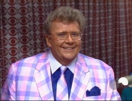 Rod is wearing a purple/pink pastel gingham jacket, matching neck tie, dark-blue shirt with white collar and dark blue pocket square
